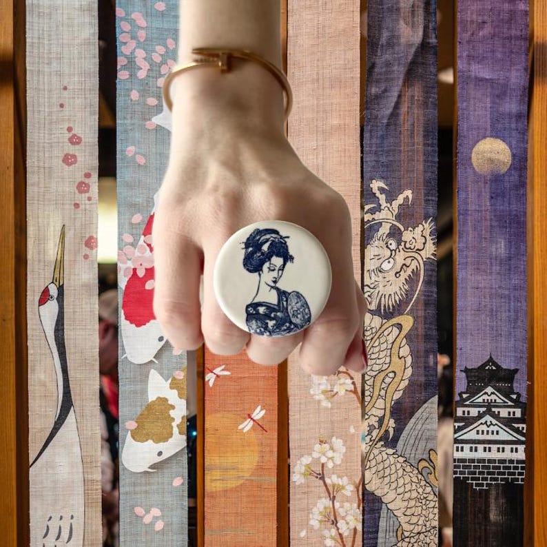 Pode incluir: Um suporte de telefone branco e azul com uma ilustra&ccedil;&atilde;o de gueixa. O suporte apresenta uma ilustra&ccedil;&atilde;o detalhada de uma gueixa em trajes tradicionais. O fundo inclui v&aacute;rios pain&eacute;is com designs de inspira&ccedil;&atilde;o japonesa.