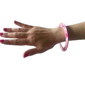 May include: A pink and white bangle bracelet with a marbled design.