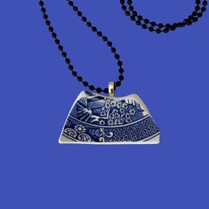 May include: A blue and white ceramic pendant with a floral design hangs from a black chain necklace.