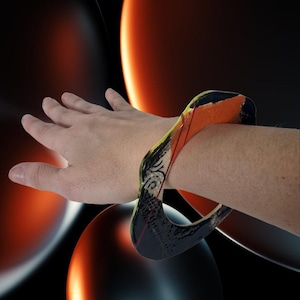 Peut inclure: Un bracelet carré avec un motif abstrait coloré. Il présente des accents orange, noirs, jaunes et blancs. Le bracelet mesure environ 6,35 cm de large et est orné de motifs.
