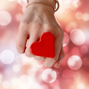 Puede incluir: Un anillo rojo en forma de corazón usado en un dedo. El anillo está hecho de un material liso y brillante y es de un rojo brillante y vibrante.