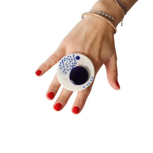 May include: A white ceramic ring with a blue and white polka dot design and a large blue circle in the centre.