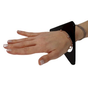 May include: A black acrylic bracelet with a unique design. The bracelet is worn on a wrist with a gold chain bracelet.