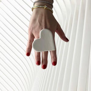 以下が含まれることがあります： 赤いマニキュアを塗った指につけられた、白いセラミック製のハート型のリング