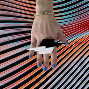 Pode incluir: Um anel de raio preto e branco. O anel é usado no dedo indicador de uma mão com esmalte de unha azul.