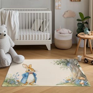Puede incluir: Alfombra rectangular con una ilustración de Peter Rabbit con chaqueta azul y pajarita roja. La alfombra, con fondo crema, presenta una escena de bosque y está colocada en una habitación infantil.