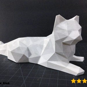 May include: A white, geometric cat sculpture in a resting pose. The cat is made of many triangular and polygonal shapes, giving it a modern, low-poly aesthetic. The sculpture is on a black surface.
