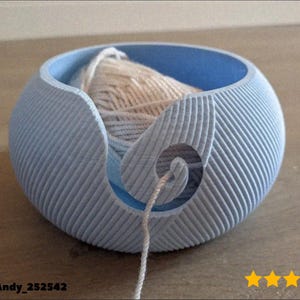 Może przedstawiać: Jasnoniebieska miska na przędzę ze spiralnym wzorem i jasną kulką przędzy w środku. Misa ma teksturowaną, żebrowaną powierzchnię zewnętrzną i gładkie, niebieskie wnętrze. Nić przędzy wychodzi przez spiralny otwór.