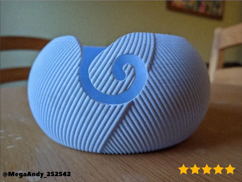 May include: A light blue yarn bowl with a spiral design. The bowl has a textured surface with vertical lines and a curved shape. The bowl is sitting on a wooden surface. The text "@MegaAndy_252542" is visible.