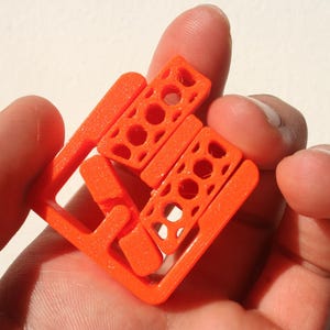 以下が含まれることがあります： 幾何学模様のオレンジ色のプラスチック製インターロッキングパズルのおもちゃ。おもちゃは、複数のピースが組み合わさって3次元の形を作ります。