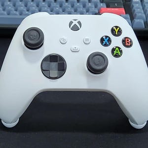 May include: A white Xbox Series X controller with black buttons and a black skull-shaped button on the left side.