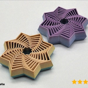 Op de afbeelding: Twee stervormige, gelaagde houten puzzels. Eén is bruin met een turquoise basis, de andere is paars met een blauwe basis. De puzzels hebben een zigzagontwerp en een stervormig gat in het midden. De Etsy shopnaam is zichtbaar.