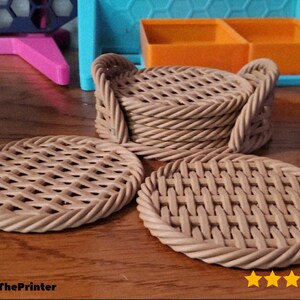 May include: A set of woven-style coasters in a light brown color. The coasters have a circular shape with a basket weave design. A stack of coasters with handles is also visible. The image includes the text "@JamesThePrinter" and a star rating.