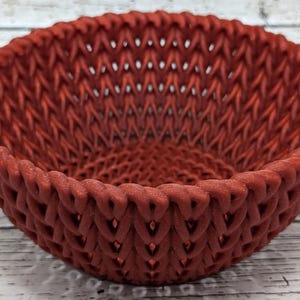 May include: A red woven bowl with a decorative pattern. The bowl is made of a textured material and has a round shape.