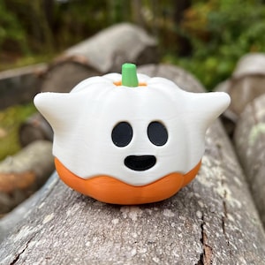 Op de afbeelding: Een witte, spookvormige pompoen met een vriendelijk gezicht en een oranje steel. De pompoen ligt op een houten oppervlak.