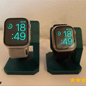 May include: Two smartwatches displayed on teal green stands. The watch faces show the time as 18:49. One watch has a silver case and a gray band, the other has a gold case and a black band.