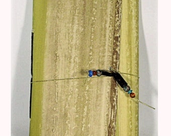 May include: A green and brown journal with a gold string closure and black and colorful beads. The journal has a textured, watercolor-like design.