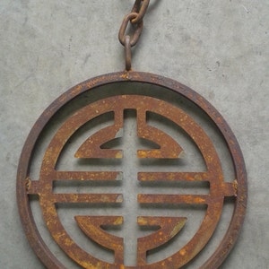 May include: A rusty metal circle with a decorative design in the center. The circle is attached to a chain with a ring at the top.