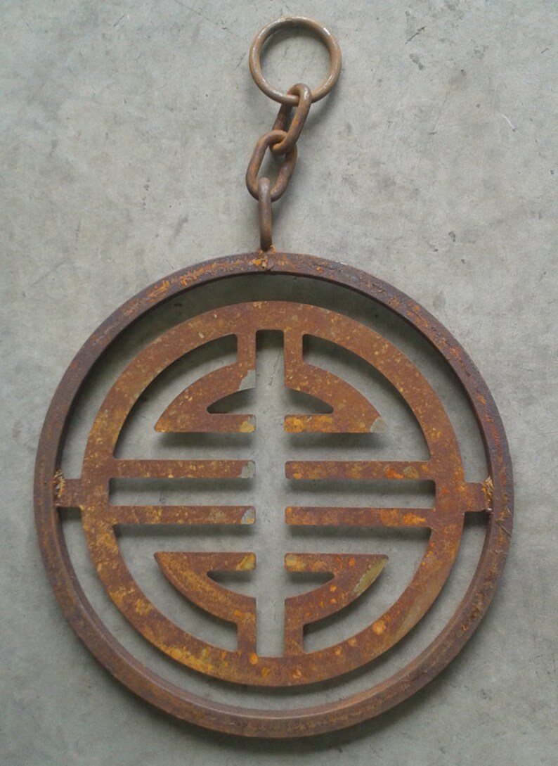 May include: A rusty metal circle with a decorative design in the center. The circle is attached to a chain with a ring at the top.