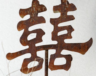 May include: A rusty metal garden stake with the Chinese character for "joy" or "happiness" in a stylized font.