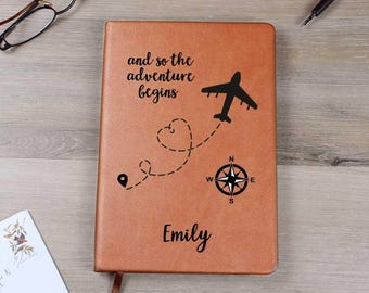 May include: Brown leather journal with the text "and so the adventure begins" and a compass and airplane graphic. The name "Emily" is personalized on the front.