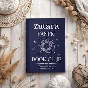 May include: A navy blue book with the title "Zutara FANFIC BOOK CLUB" in white text. The book features a white sun and moon design with stars. The text "You rise with the moon, I rise with the sun" is printed below the design.