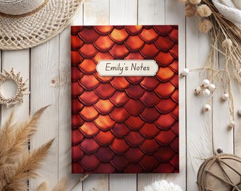 May include: A red notebook with a scale pattern cover and the text "Emily's Notes" on a white label.