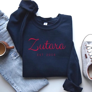 May include: A navy blue sweatshirt with the text "Zutara Est 2005" in red lettering.