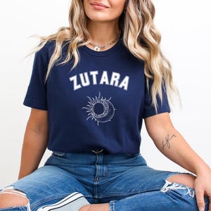May include: A navy blue t-shirt with white text that reads "ZUTARA" and a white sun and moon graphic.