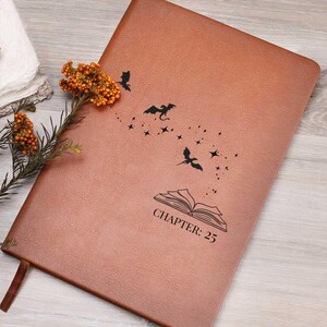 May include: A brown leather-bound journal with a decorative design of flying bats and stars. The text "CHAPTER: 25" is printed below an open book illustration. A brown ribbon bookmark is visible.