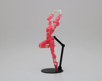 May include: A pink articulated action figure with white accents is posed in a dynamic stance on a black stand. The figure has a segmented body and limbs, allowing for a wide range of poses.
