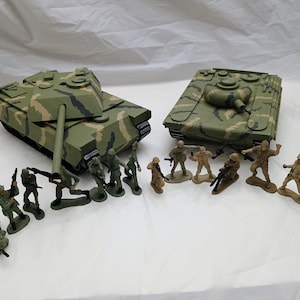 Op de afbeelding: Twee camouflage speelgoed tanks met een groep plastic speelgoed soldaten. De soldaten staan in verschillende poses en houden wapens vast. De tanks zijn beide groen en bruin met een camouflage patroon.
