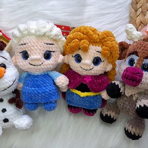 May include: A collection of crocheted dolls featuring characters from a popular animated film. The dolls include Olaf, Elsa, Anna, and a reindeer, crafted from soft yarn in various colours, with detailed facial features and clothing.