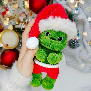 May include: A green plush Grinch doll wearing a red Santa hat, red shorts, and a white trim. The Grinch has blue eyes and a white pom-pom on the hat. The doll is a Christmas-themed item.