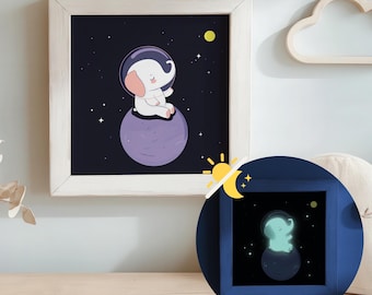 Può includere: Un elefante bianco con un casco spaziale siede su un pianeta viola in uno spazio blu scuro con stelle. L'immagine è in una cornice bianca. Un'immagine più piccola dell'elefante in una cornice blu mostra l'elefante che brilla al buio.