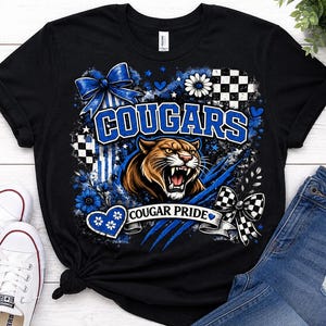 Könnte beinhalten: Ein schwarzes Kurzarm-T-Shirt mit einem Grafikdruck eines fauchenden Pumas, dem Text COUGARS und COUGAR PRIDE, blauen Schleifen, Karomustern, Blumen und Herzen. Das Design enthält zudem blaue Krallenspuren und Sternakzente.