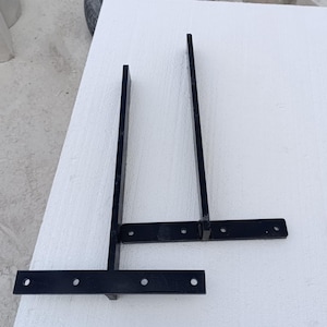 May include: Two black metal brackets with multiple holes. The brackets are connected together with a horizontal bar.
