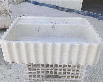 May include: White marble sink with a wavy edge. The sink is sitting on a white plastic crate.
