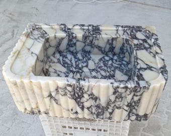 May include: A white marble sink with a decorative fluted edge and a purple and white marbled interior.
