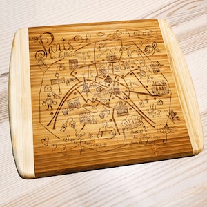 May include: A wooden cutting board with a laser-engraved map of Paris, France. The map includes landmarks like the Eiffel Tower, Arc de Triomphe, and Montmartre. The text "Ooh la la!" is also engraved on the board.