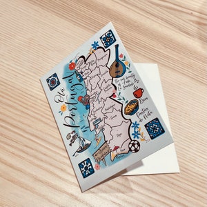 May include: A colorful illustrated map of Portugal with various landmarks and symbols. The map is on a white background with a blue border. The text "Olá Portugal" is written in a cursive font at the top of the map. The map includes the cities of Porto, Lisbon, Coimbra, and Algarve. The map also includes symbols for a guitar, a rooster, a soccer ball, and a pastry.