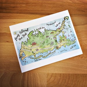 May include: A hand-drawn map of Long Island, New York, with a blue outline and green interior. The map shows major towns and cities, including Montauk Point, Port Jefferson, and Huntington Bay. The map also includes a compass rose and the words "Long Island, New York" in a handwritten font.