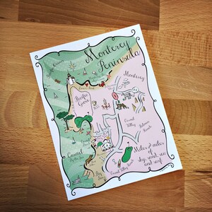 May include: A hand-drawn map of the Monterey Peninsula in California, featuring landmarks like Pacific Grove, Carmel-by-the-Sea, and Carmel Valley Ranch. The map is illustrated with whimsical details like a whale, a lighthouse, and a glass of wine.