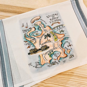 May include: A hand-drawn map of Marco Island, Florida, with a blue and white striped border. The map shows the location of Collier Bay, Tigertail Beach, City Beach, Robert's Bay, and Barfield Bay. The map also shows the location of Marco Road, Winterberry Drive, and the Isles of Capri. The text "Welcome to Marco Island!" is written in a cursive font at the top of the map.