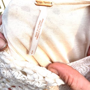 Puede incluir: Primer plano de un vestido color crema con ribete de encaje. El vestido tiene una etiqueta que dice "Free People" y "Hecho en Vietnam". La talla es peque&ntilde;a.