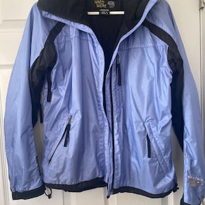 May include: A light blue and black hooded jacket with the text "Mountain Hardwear" on the front. The jacket has a zipper closure and two pockets on the front.