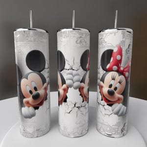 May include: Three stainless steel tumblers featuring Mickey and Minnie Mouse. The tumblers have a white background with a comic strip design and a cracked wall effect. Mickey Mouse is on one tumbler, and Minnie Mouse is on another, with a red polka dot bow.