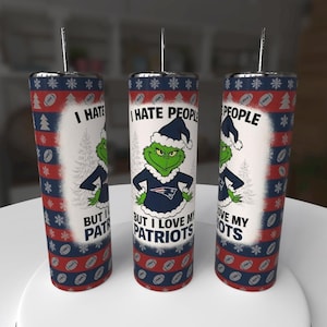 May include: Three stainless steel tumblers with Grinch and Patriots-themed designs. Each tumbler features the Grinch in a Patriots uniform, with text that reads "I HATE PEOPLE BUT I LOVE MY PATRIOTS". The tumblers have a red, white, and blue color scheme.