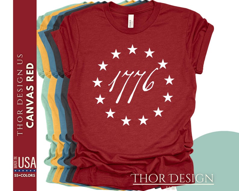 Pode incluir: Camiseta de lona vermelha com um c&iacute;rculo branco de estrelas e o texto "1776" no centro. A camiseta &eacute; feita nos Estados Unidos e est&aacute; dispon&iacute;vel em 55 cores.