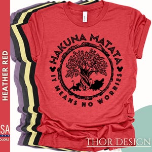 Puede incluir: Camiseta roja con un gr&aacute;fico circular negro que presenta un &aacute;rbol, las palabras "Hakuna Matata" y la frase "It means no worries".